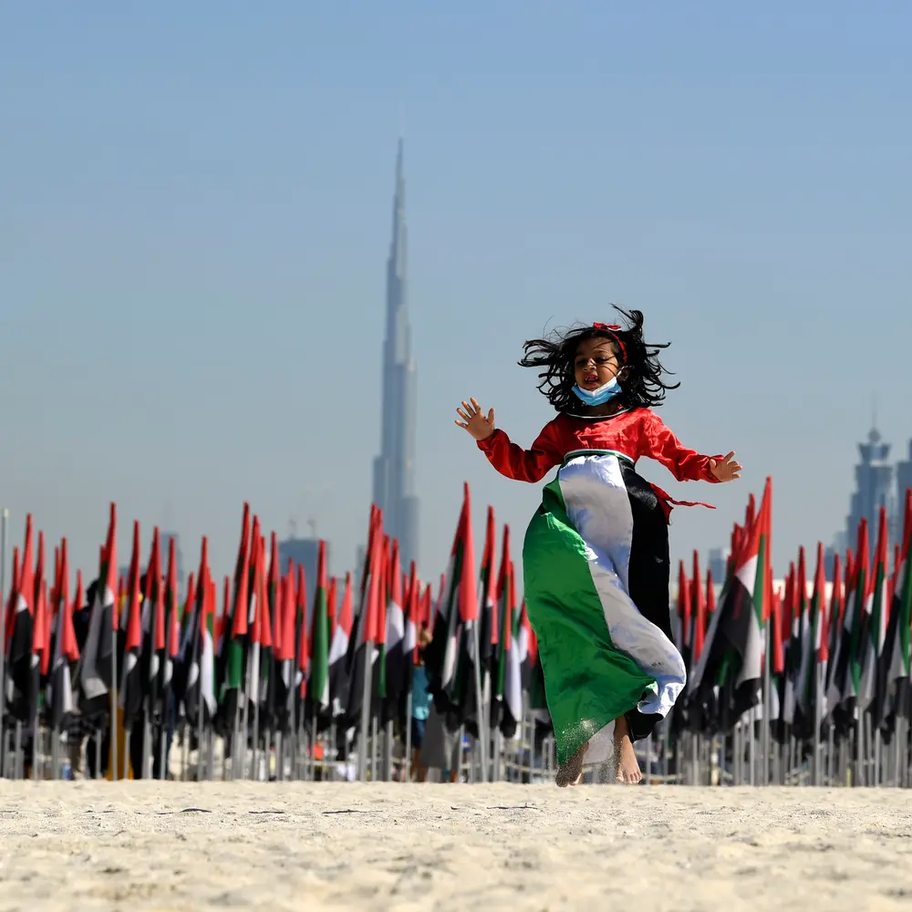 Child jumping with UAE flags and city skyline.