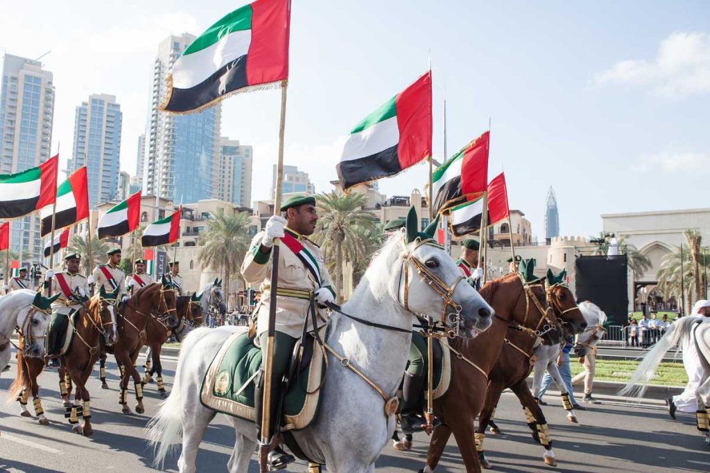 Horsemen with UAE flags in urban parade.